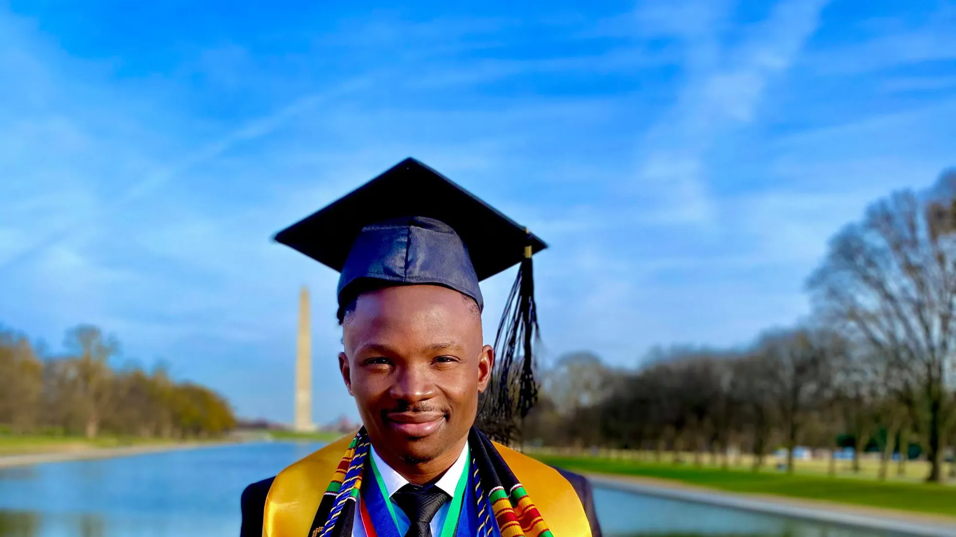 A New Futures college graduate poses in his regalia in front of the reflecting pond and the Washington Monument in Washington, D.C.
