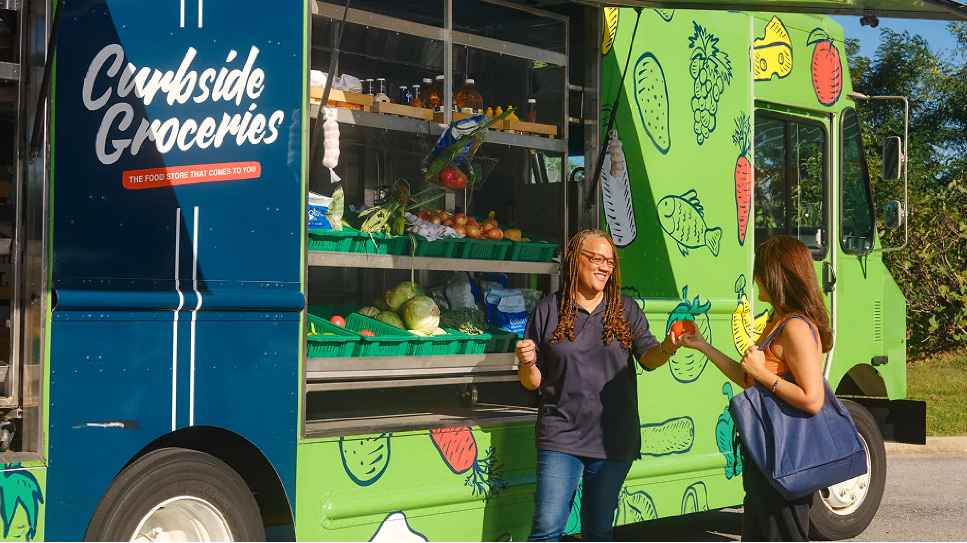 Two women stand outside a bright green grocery truck labeled "Curbside Groceries." One woman smiles at the other while she hands her a tomato.