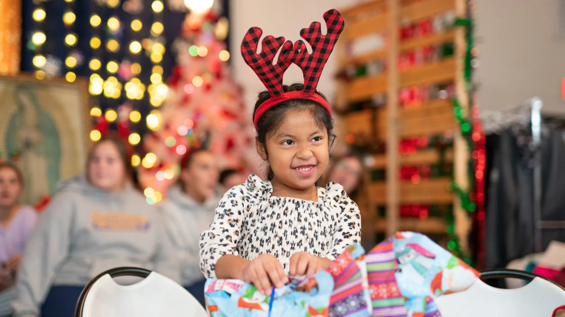 A young girl in front of a christmas tree opening a gift.