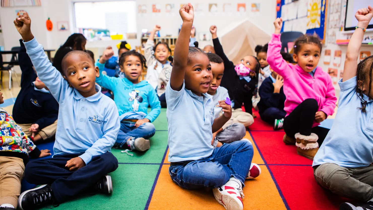 A group of school children raising their hands.
