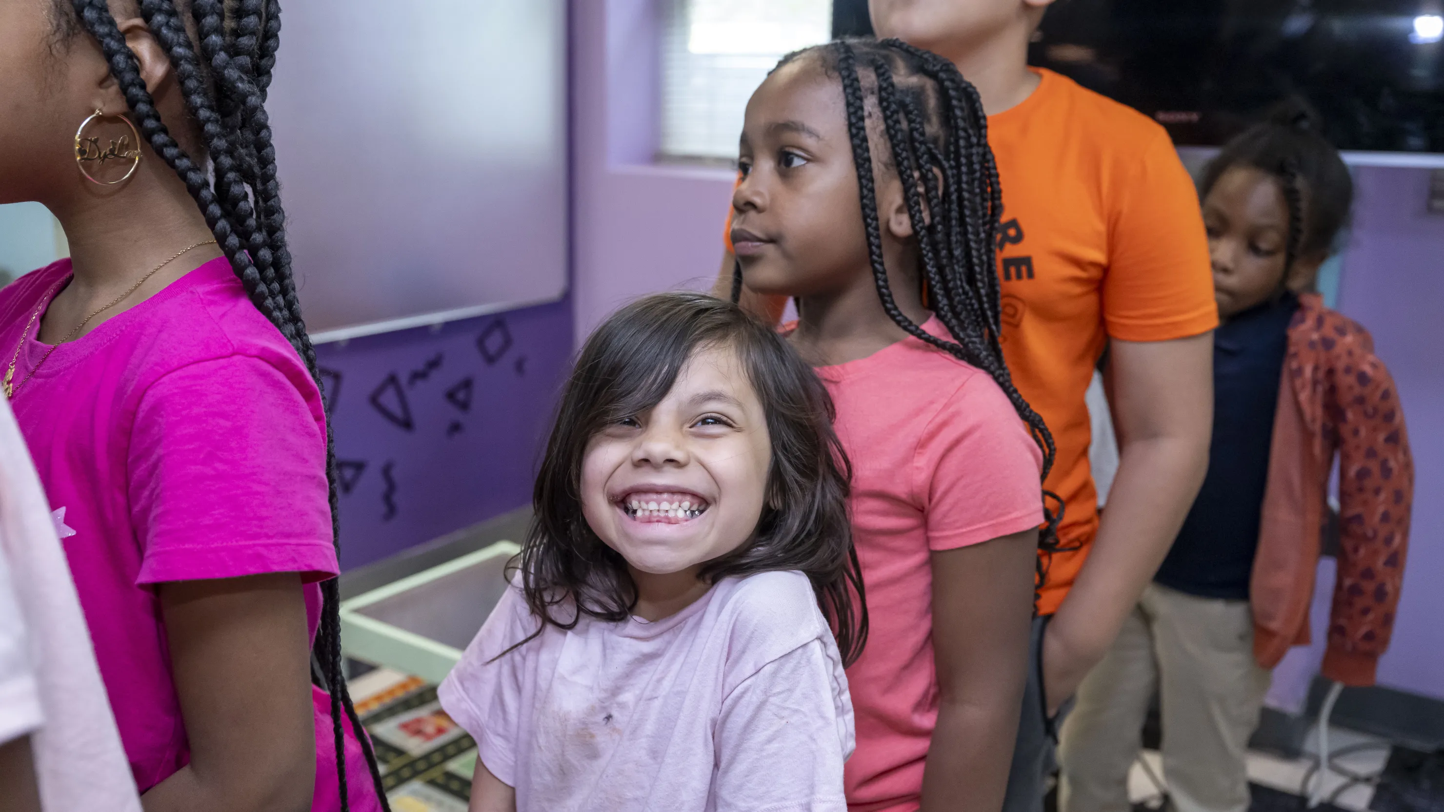 Children wait in line. A young girl, center, smiles eagerly at the camera.