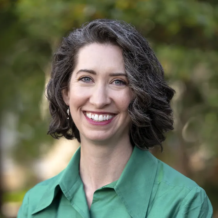 A professional headshot of Sarah Elbert. She has brown chin-length hair and wears a green dress.