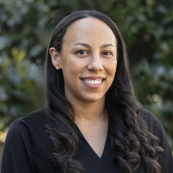 A professional headshot of Ashley Davis. She has brown hair past her shoulders and wears a black v-neck dress.
