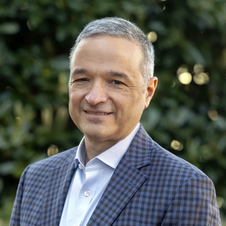 A professional headshot of Joe Del Guercio. He has short salt and pepper hair and wears a blue checkered blazer with a blue shirt underneath.