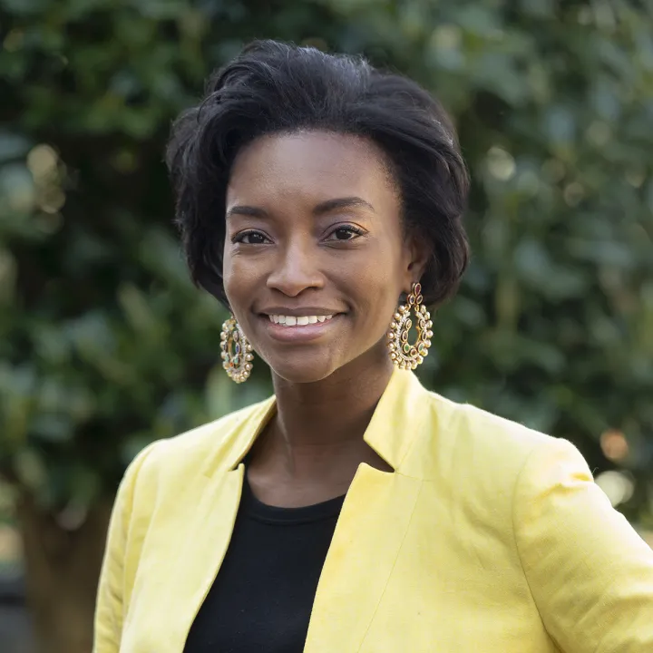 A professional headshot of Natalie Grandison. She has chin-length brown hair and wears a yellow blazer over a black shirt.