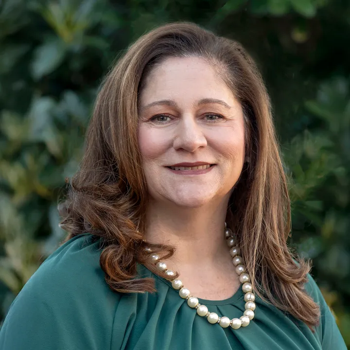 A professional headshot of Chris Jones. She has brown shoulder-length hair and wears a green blouse with a white pearl necklace.