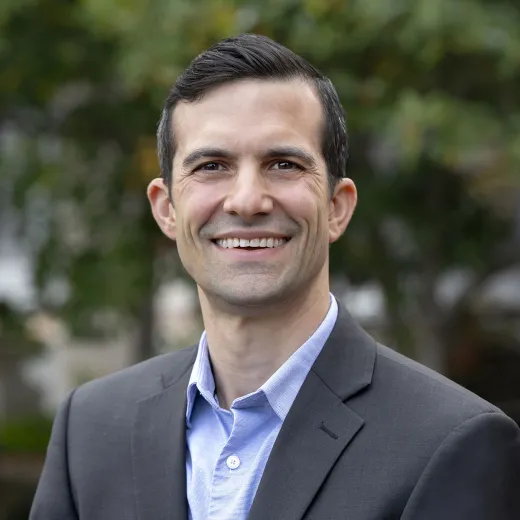 A professional headshot of Andrew Knutson. He wears a black blazer and a blue shirt.
