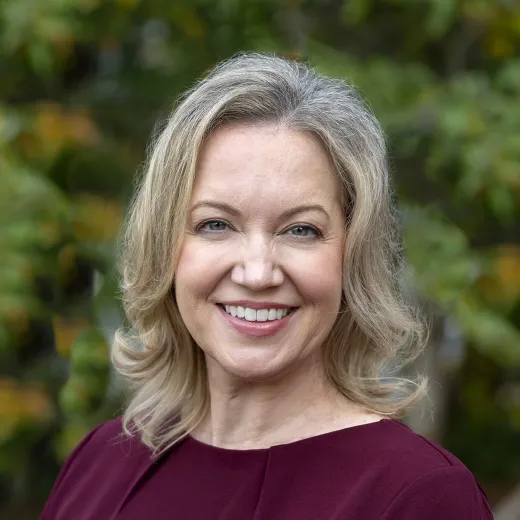 A professional headshot of Danielle Hamberger. She has blonde shoulder-length hair and wears a burgundy dress.