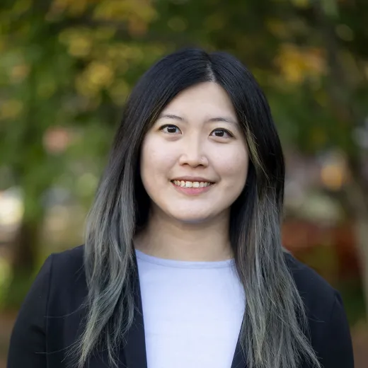 A professional headshot of Joan Zhang. She has long dark hair and wears a blue shirt and black sweater.