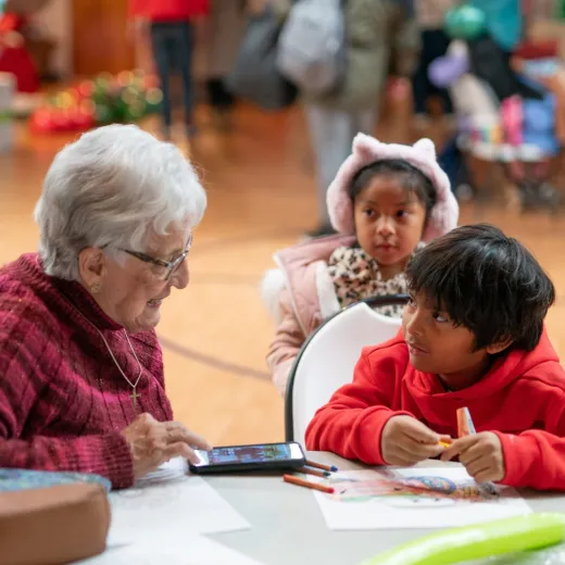An older woman, left, speaks with two young children as they do a craft in a school gymnasium.
