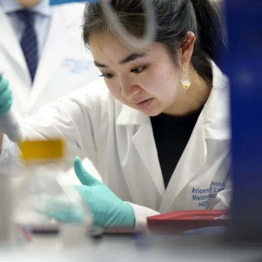  A researcher conducts an experiment in a lab. She wears a white lab coat and protective gloves.