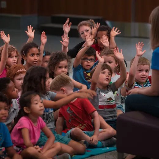 An group of elementary schoolchildren raise their hands to answer a question from a teacher.