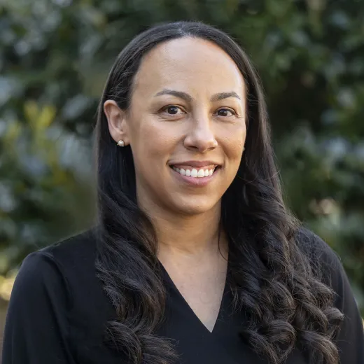 A professional headshot of Ashley Davis. She has brown hair past her shoulders and wears a black v-neck dress.
