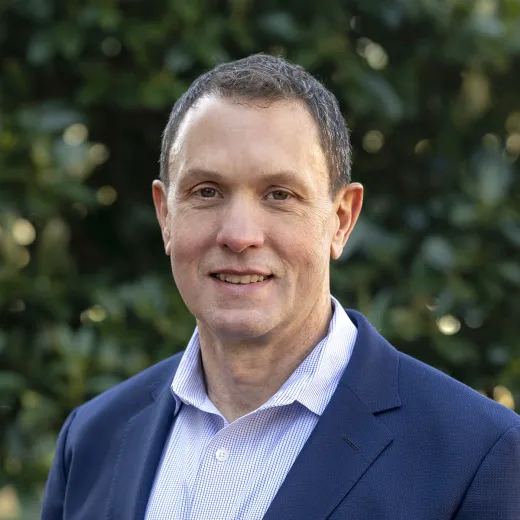 A professional headshot of Mike Monroe. He has short brown hair and wears a navy blazer over a blue shirt.