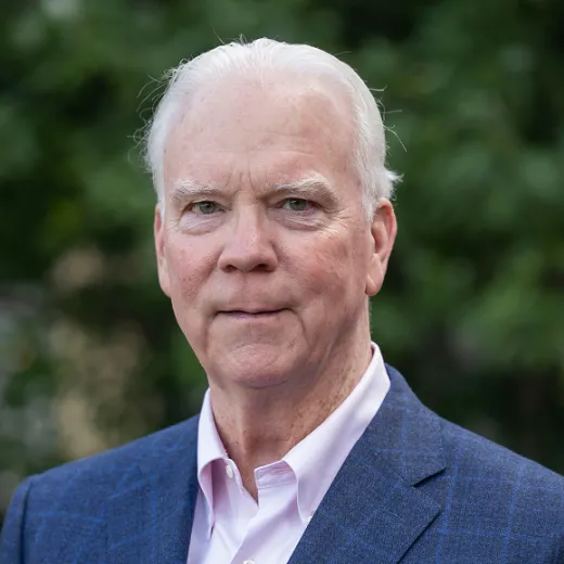 A professional headshot of Board Director Robert Flanagan. He wears a blue blazer and a pink shirt.