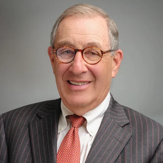 A professional headshot of Larry Nussdorf. He wears glasses, a grey blazer and an orange tie.