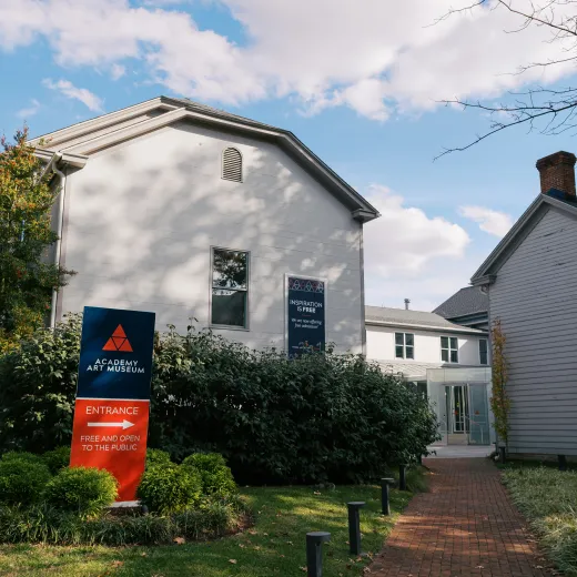 The Academy Art Museum, a white building shaded by trees, set against a blue sky with white clouds.