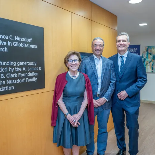 Melanie Nussdorf, Joe Del Guercio and Ingo Mellinghoff, MD stand next to signage for The Lawrence C. Nussdorf Initiative in Glioblastoma Research.