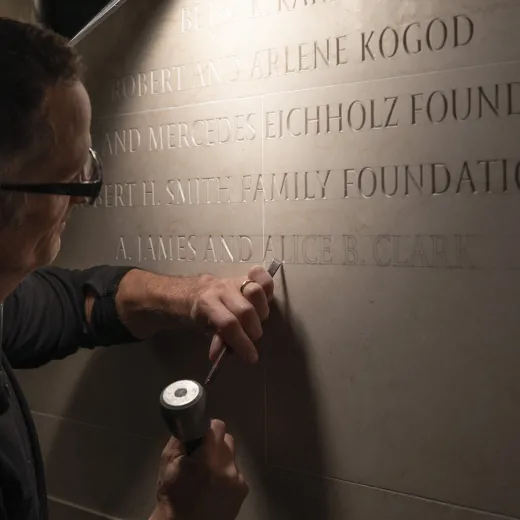 An engraver etches the names 'A. James and Alice B. Clark' into a stone wall at the National Gallery of Art.