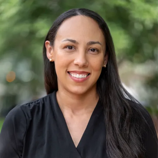 A professional headshot of Ashley Davis. She has brown hair past her shoulders and wears a black v-neck dress.