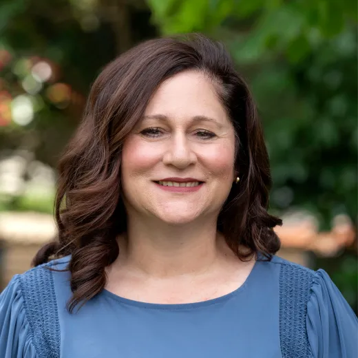 A professional headshot of Chris Jones. She has brown shoulder-length hair and wears a green blouse with a white pearl necklace.
