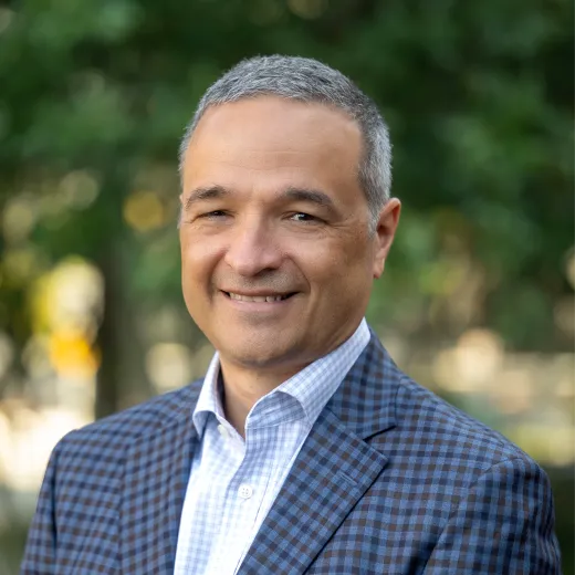 A professional headshot of Joe Del Guercio. He has short salt and pepper hair and wears a blue checkered blazer with a blue shirt underneath.