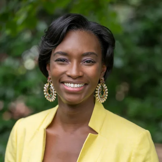 A professional headshot of Natalie Grandison. She has chin-length brown hair and wears a yellow blazer over a black shirt.