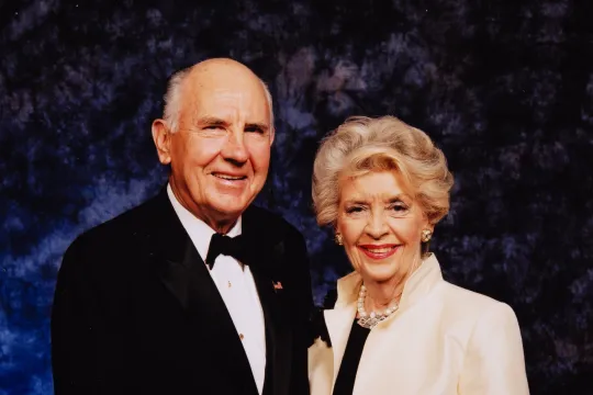 A. James and Alice B. Clark attend a black tie gala. They are in their seventies and hold hands while they pose.