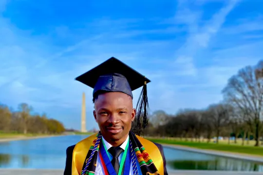 A New Futures college graduate poses in his regalia in front of the reflecting pond and the Washington Monument in Washington, D.C.
