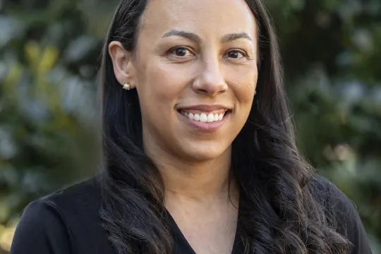 A professional headshot of Ashley Davis. She has brown hair past her shoulders and wears a black v-neck dress.