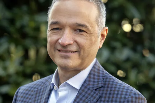 A professional headshot of Joe Del Guercio. He has short salt and pepper hair and wears a blue checkered blazer with a blue shirt underneath.