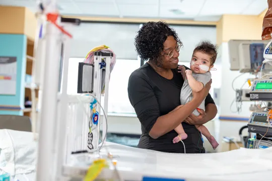 A mother holds her newborn baby proudly in a hospital room.