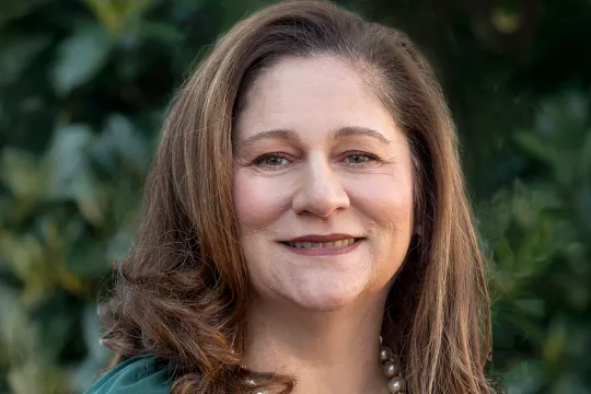 A professional headshot of Chris Jones. She has brown shoulder-length hair and wears a green blouse with a white pearl necklace.
