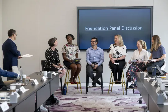Seven Clark Foundation team members are at the front of a meeting room on a panel. They laugh as they answer questions.