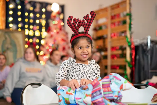 A young girl in front of a christmas tree opening a gift.