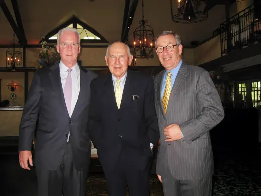 Robert Flanagan and Larry Nussdorf pose on either side of A. James Clark at a reception. They are all wearing ties and dark suits.