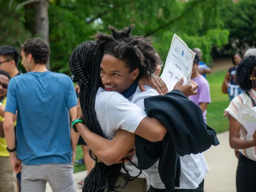 Two university students hug amongst a crowd of students greeting each other on campus.