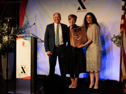 Board Chair Courtney Clark Pastrick stands on a stage and accepts an award from Headstrong, between two grantee leaders.