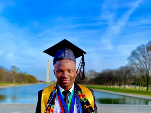 A New Futures college graduate poses in his regalia in front of the reflecting pond and the Washington Monument in Washington, D.C.