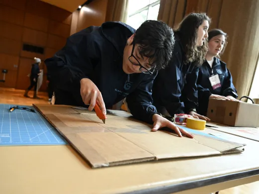 Clark Scholars participate in a design challenge. Two speak to each other while a third cuts cardboard with precision.