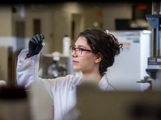 Vanderbilt Clark Scholar Yoanna Ivanova examines a test tube in a lab. She wears a white lab coat and protective gloves.