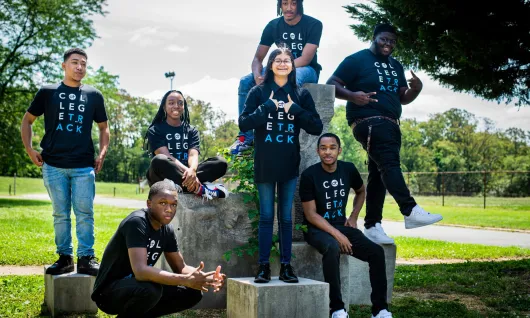 College Track students pose around a statue in a park.
