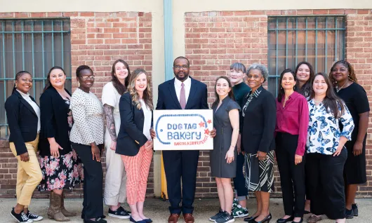 Graduates of the Dog Tag Bakery fellowship stand in a group wearing business clothes and smiling proudly.