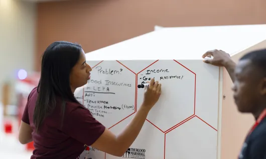 Two students draft ideas on a white board.