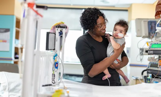 A mother holding and smiling at her baby in a hospital room.
