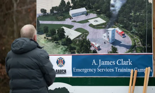 A man sits viewing signage displaying an architectural rendering of the A. James Clark Emergency Services Training Campus in Easton, Maryland.