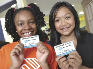 Two young girls smile and proudly display their Boys & Girls Club membership cards