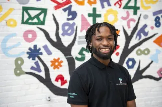 Literacy Lab Leading Men Fellow Malachi Byrd smiles in front of a colorful elementary school mural