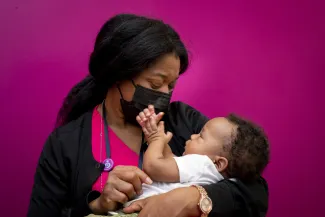 A masked healthcare professional gently cradles a happy infant baby