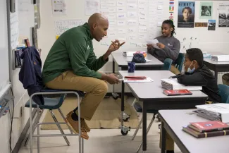 A teacher engages with a student in a classroom. Both are smiling.